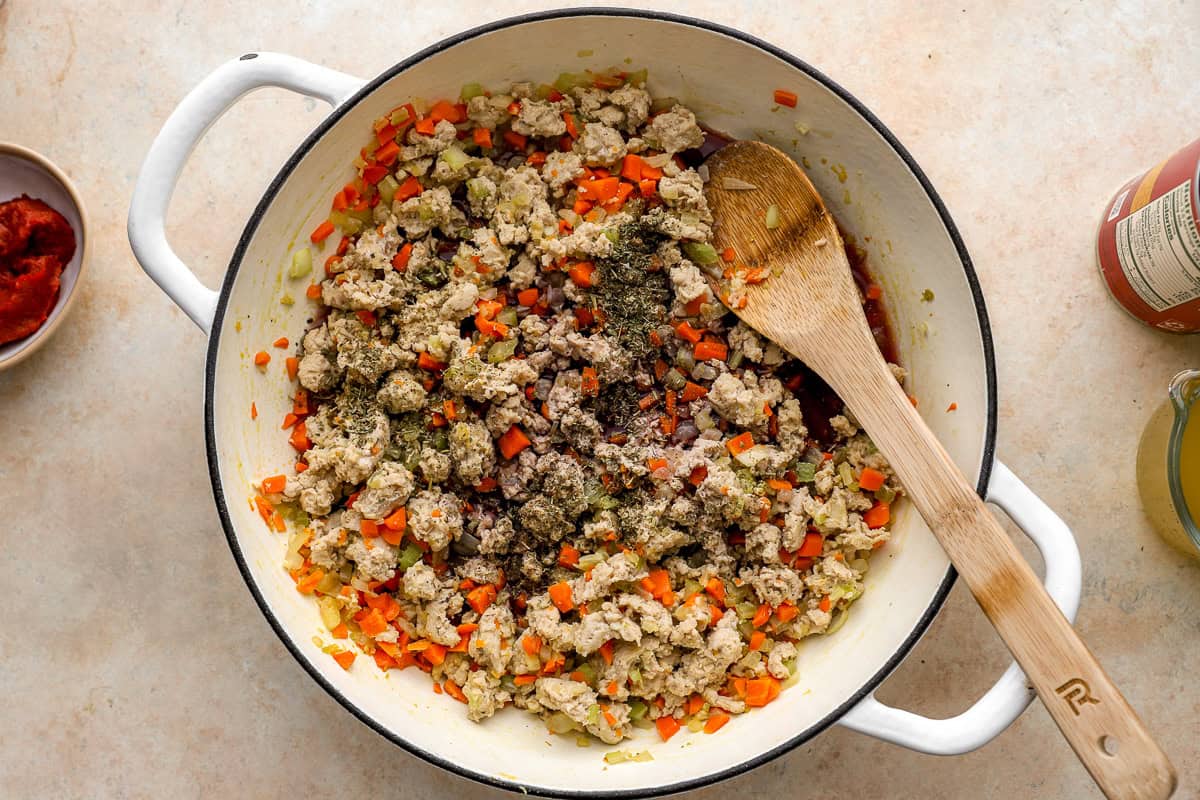 cooking ground chicken and mirepoix in a dutch oven with a wooden spoon.