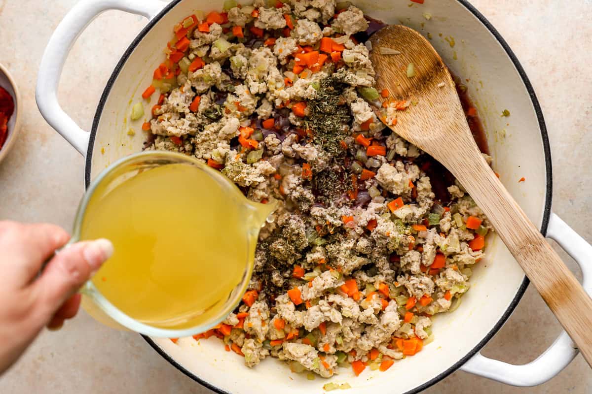 pouring chicken broth over seasoned ground chicken and vegetables in a dutch oven.