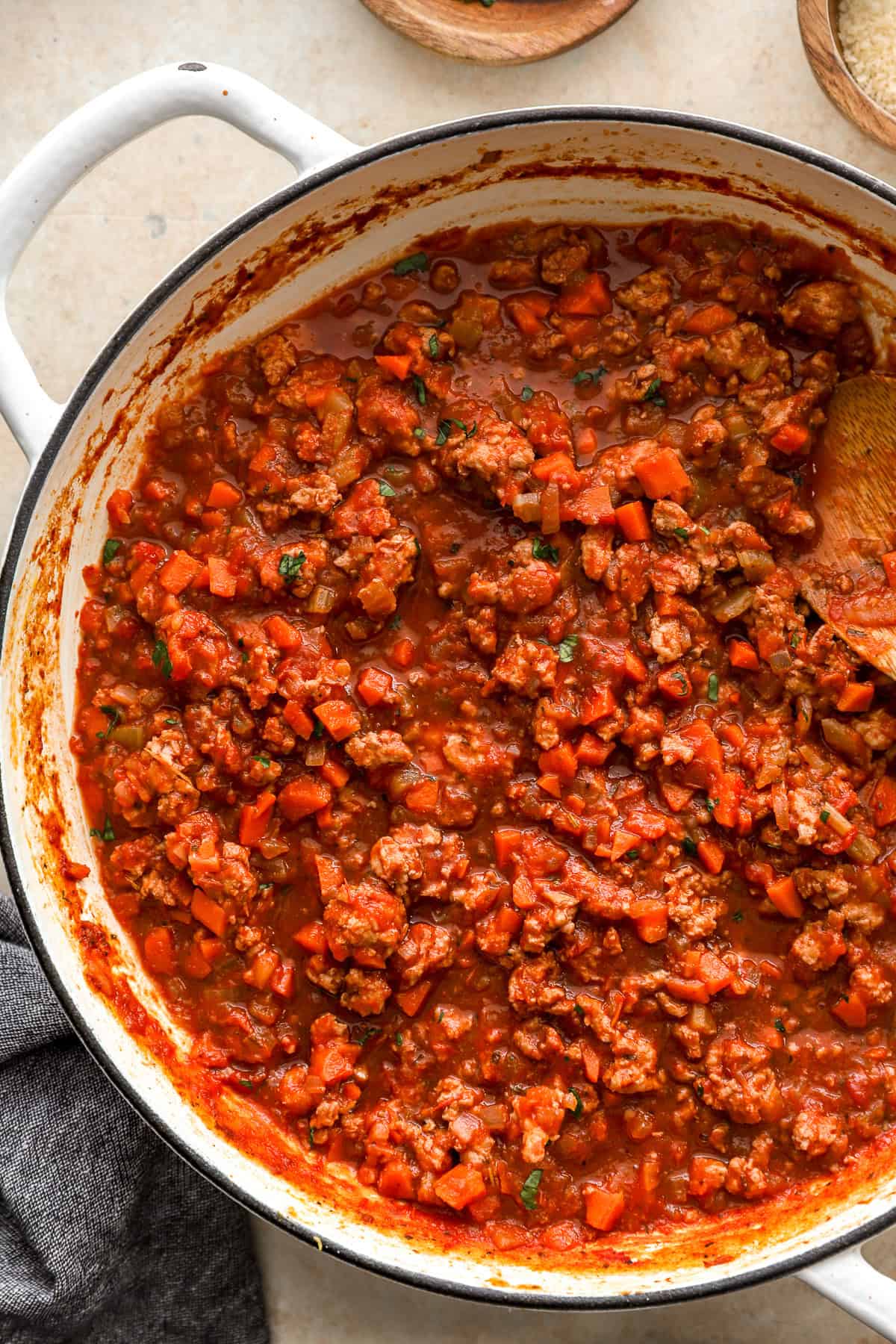 cropped view of ground chicken bolognese sauce in a dutch oven with a wooden spoon.