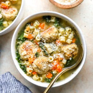 overhead view of a bowl of chicken meatball wedding soup with a spoon, topped with grated Parmesan cheese.
