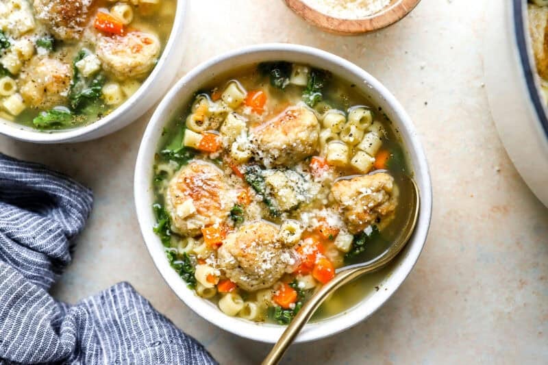 overhead view of a bowl of chicken meatball wedding soup with a spoon, topped with grated Parmesan cheese.
