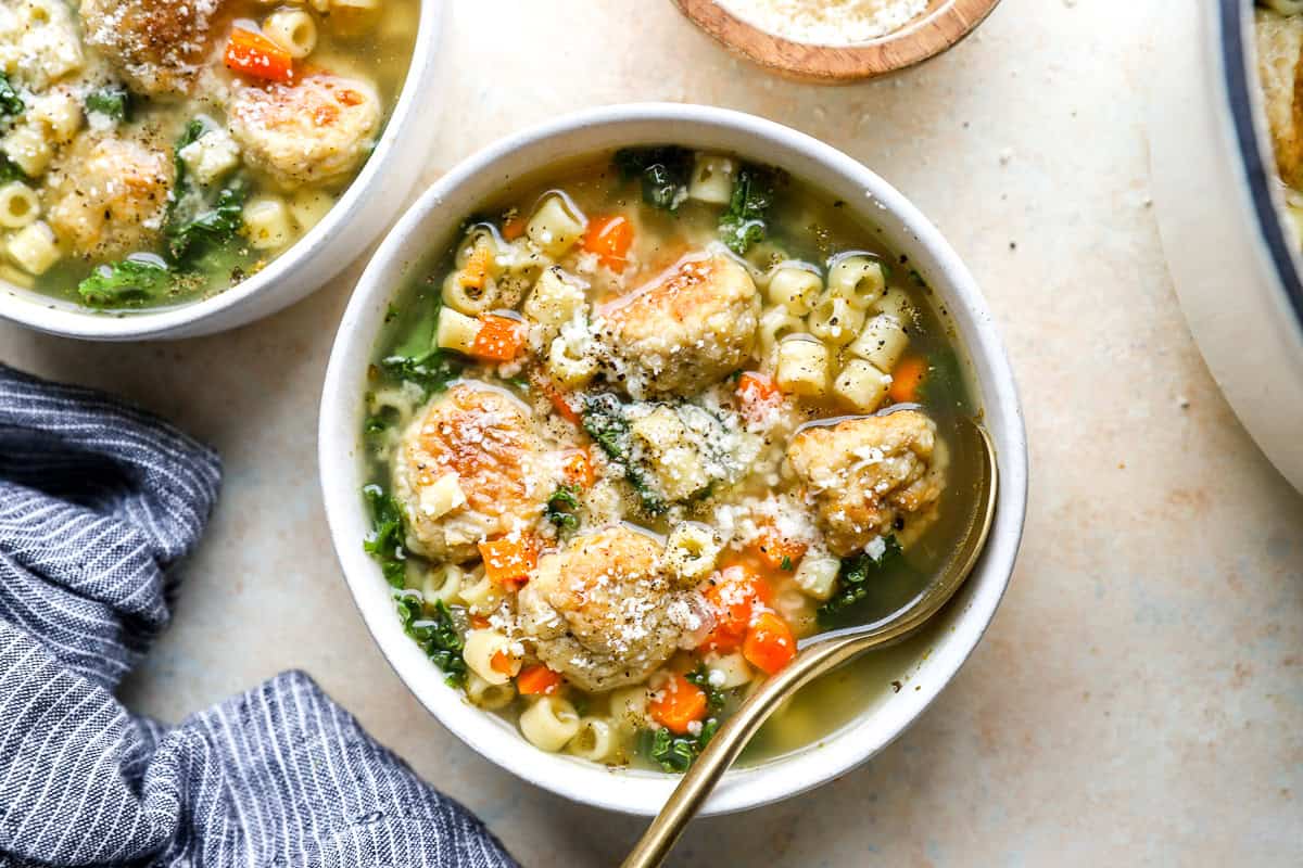 overhead view of a bowl of chicken meatball wedding soup with a spoon, topped with grated Parmesan cheese.