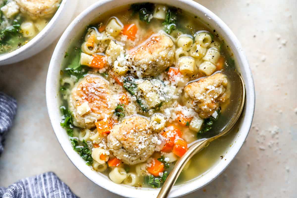 closeup overhead view of a serving of Italian chicken wedding soup in a bowl with a spoon, topped with Parmesan cheese.