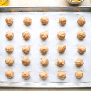 25 small ground chicken meatballs on a lined baking sheet before baking.