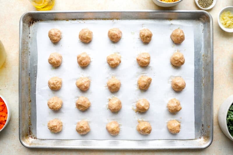 25 small ground chicken meatballs on a lined baking sheet before baking.