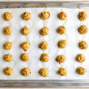 25 baked ground chicken meatballs on a lined baking sheet.
