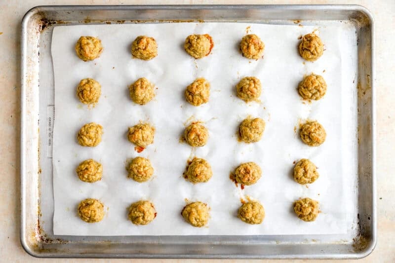 25 baked ground chicken meatballs on a lined baking sheet.