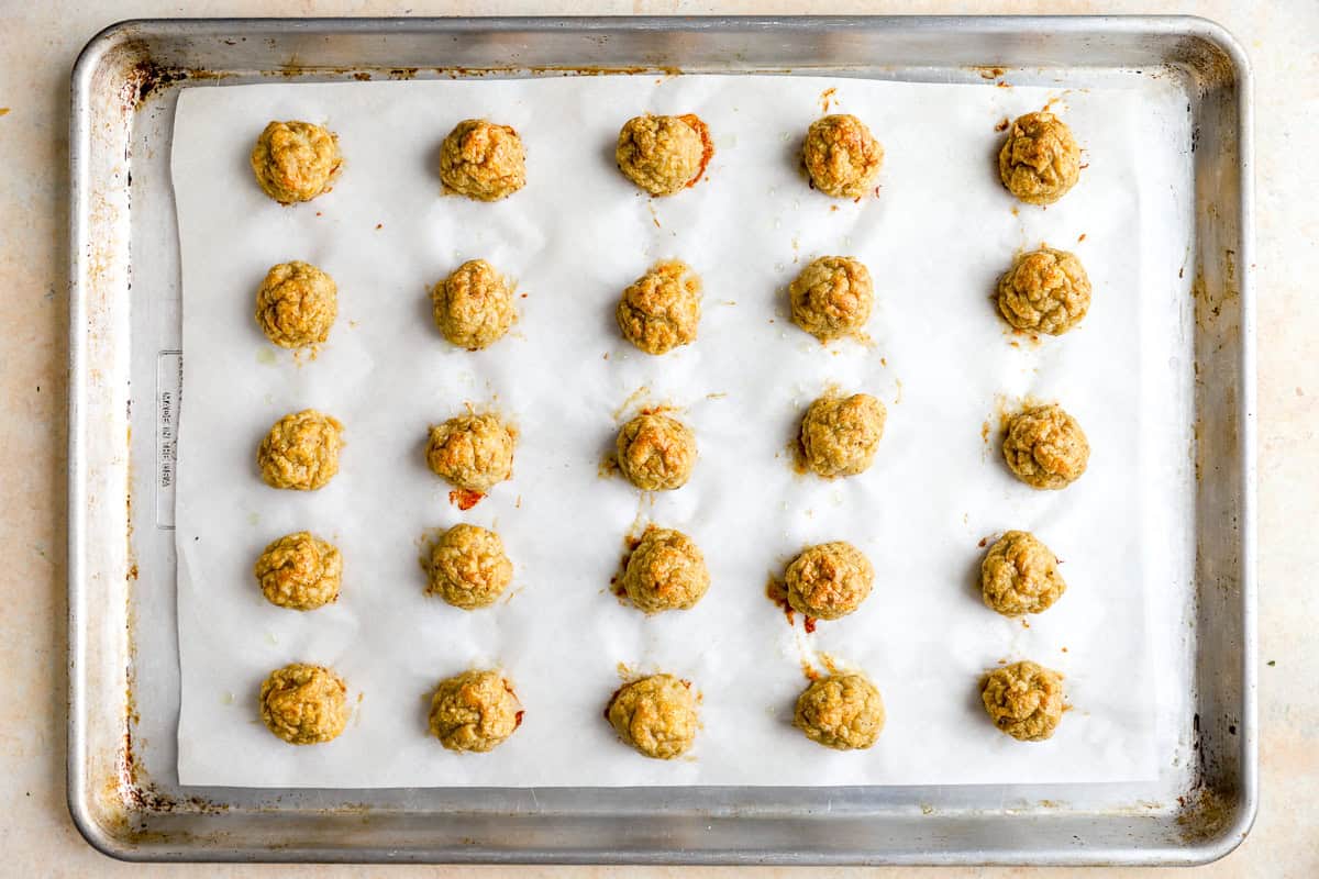 25 baked ground chicken meatballs on a lined baking sheet.