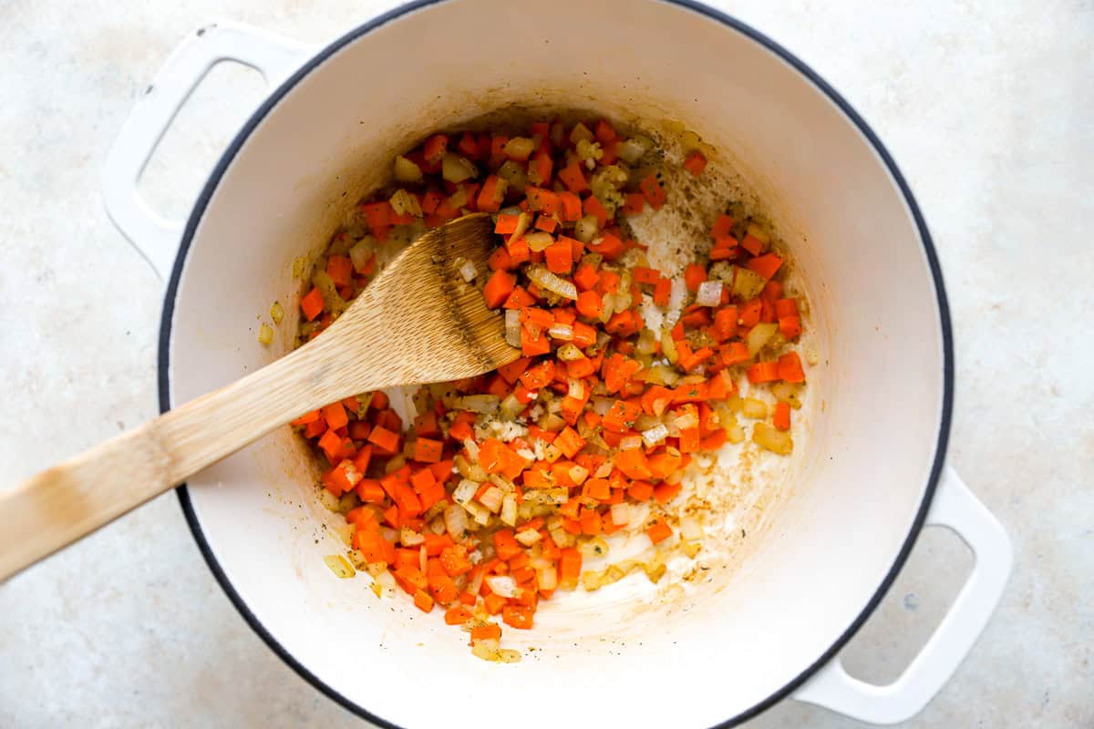 sauteeing mirepoix in a Dutch oven with a wooden spoon.