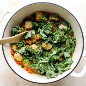 stirring kale into chicken meatball soup in a Dutch oven with a wooden spoon.