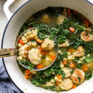 lifting a ladleful of chicken meatball soup from a Dutch oven.