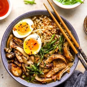overhead view of a bowl of chicken ramen with a boiled egg, green onions, and chopsticks.