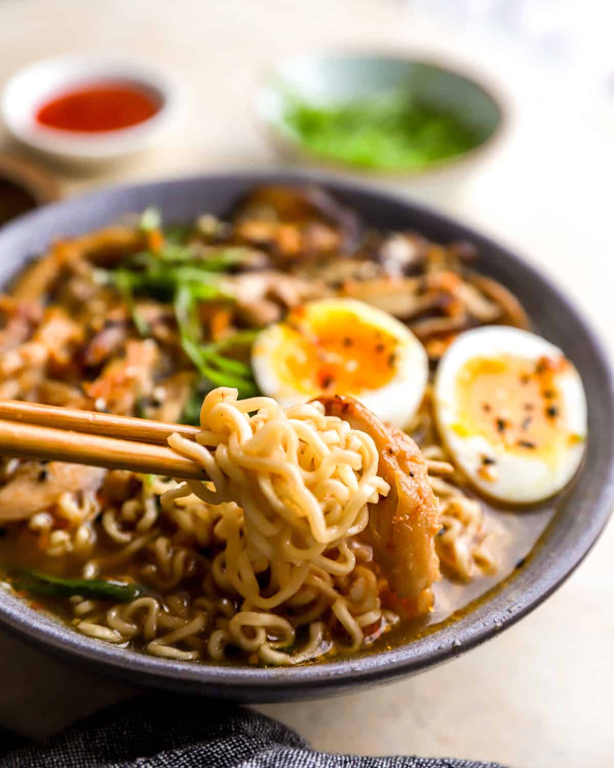 three-quarters view of a bowl of chicken ramen with chopsticks lifting some of the noodles.