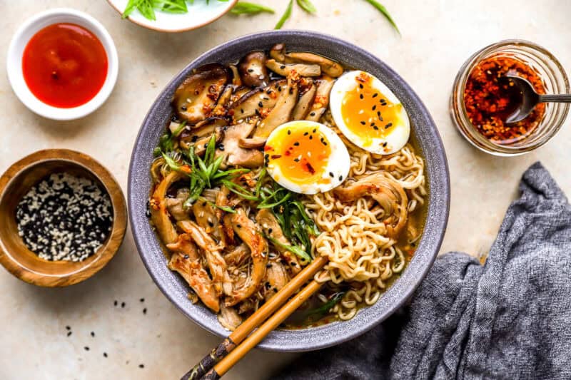 overhead view of a bowl of chicken ramen with a boiled egg, green onions, and chopsticks.