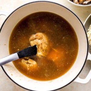 adding seared chicken thighs to shoyu ramen broth in a dutch oven.