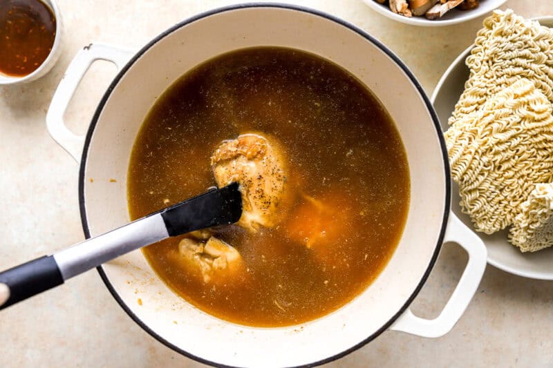 adding seared chicken thighs to shoyu ramen broth in a dutch oven.