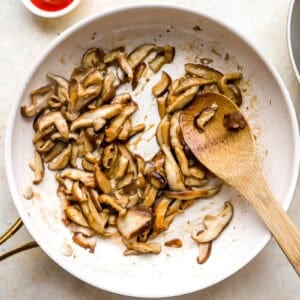 sautéeing mushrooms in a skillet with a wooden spoon.