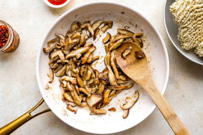 sautéeing mushrooms in a skillet with a wooden spoon.