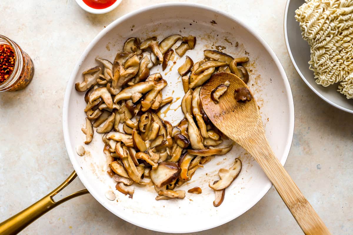 sautéeing mushrooms in a skillet with a wooden spoon.