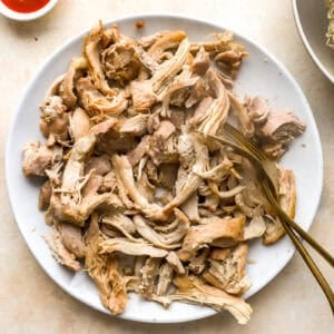 shredding chicken thighs on a plate with two forks.