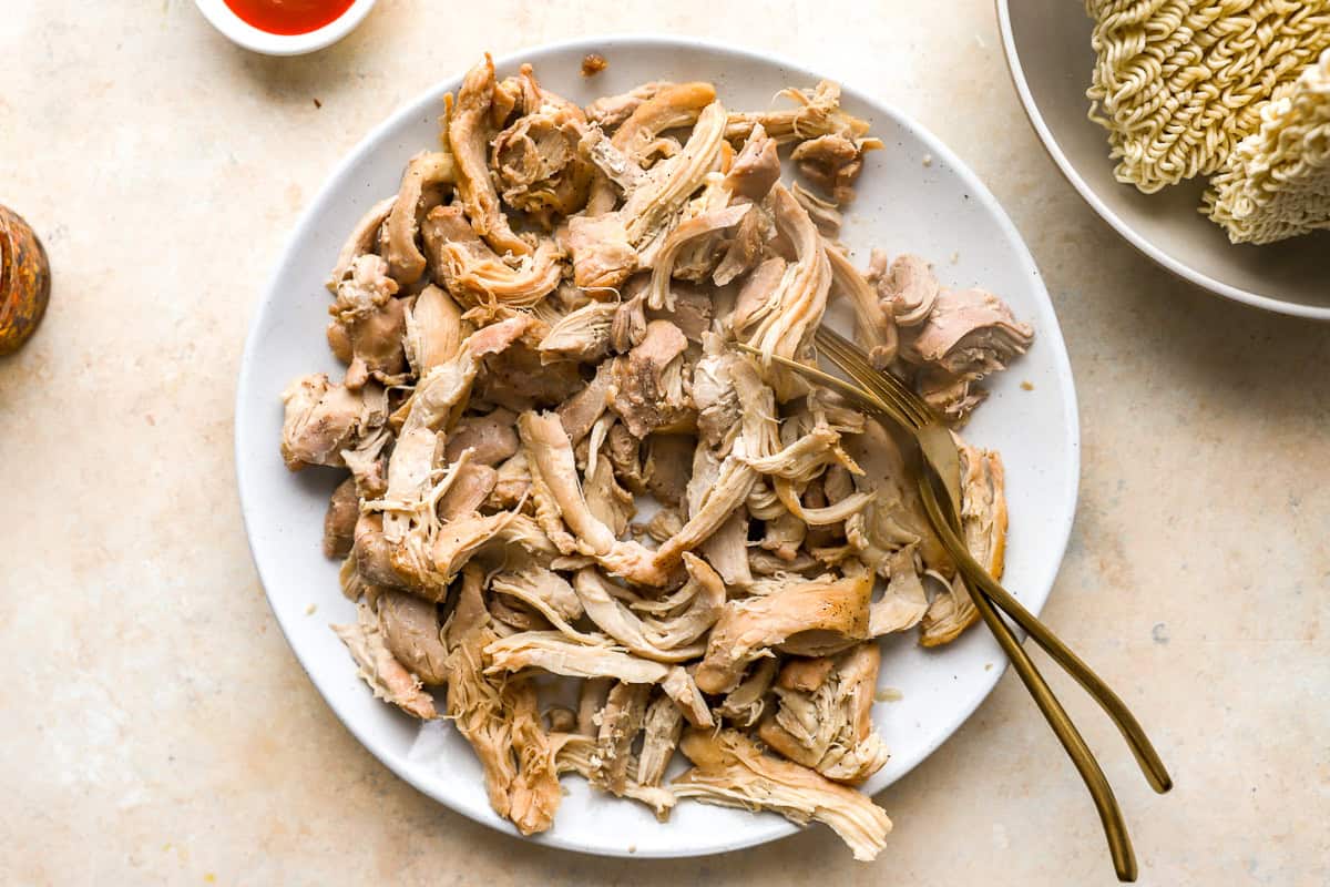 shredding chicken thighs on a plate with two forks.