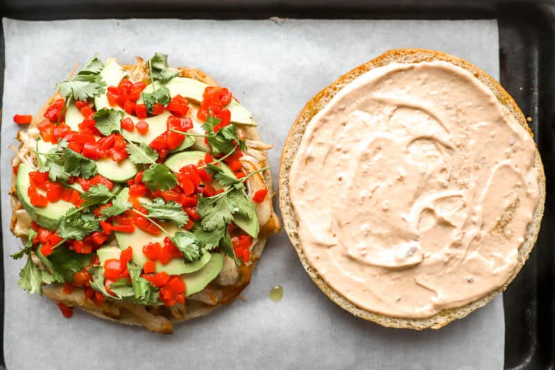 a halved focaccia round topped with shredded chicken, cheese, avocado, pimentos, and cilantro; chipotle mayo on the other half.