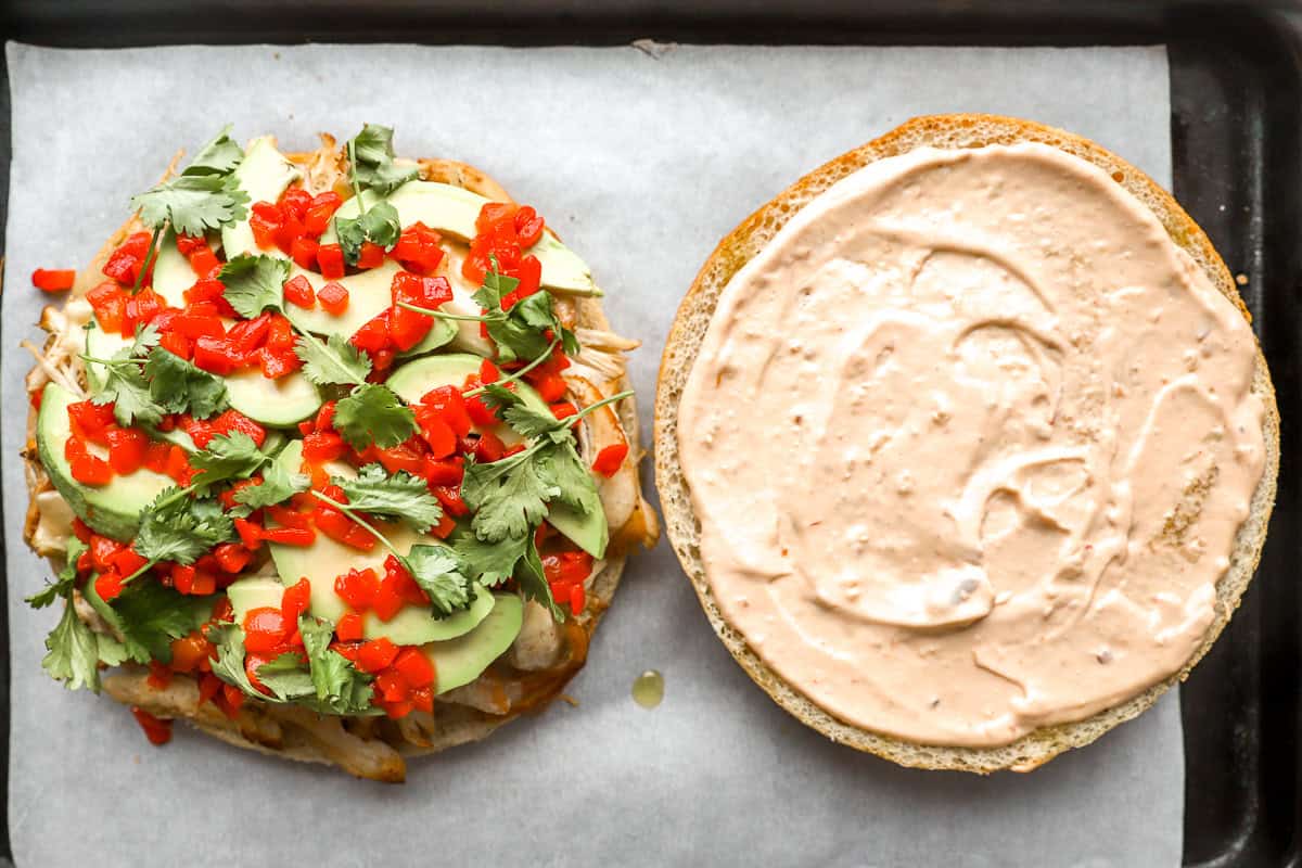 a halved focaccia round topped with shredded chicken, cheese, avocado, pimentos, and cilantro; chipotle mayo on the other half.
