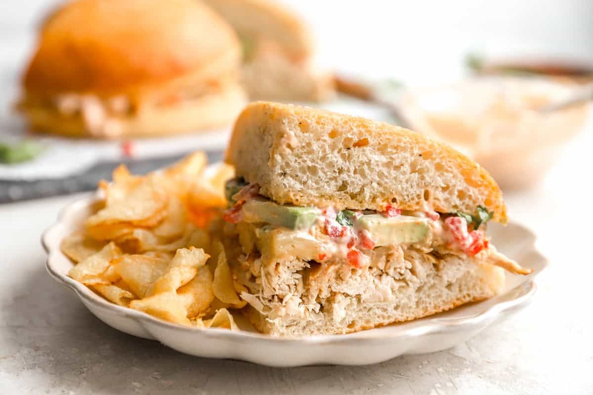 a chicken avocado sandwich on a plate with chips.