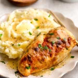 three-quarters view of creamy chicken and mashed potatoes with gravy on a plate with a fork.