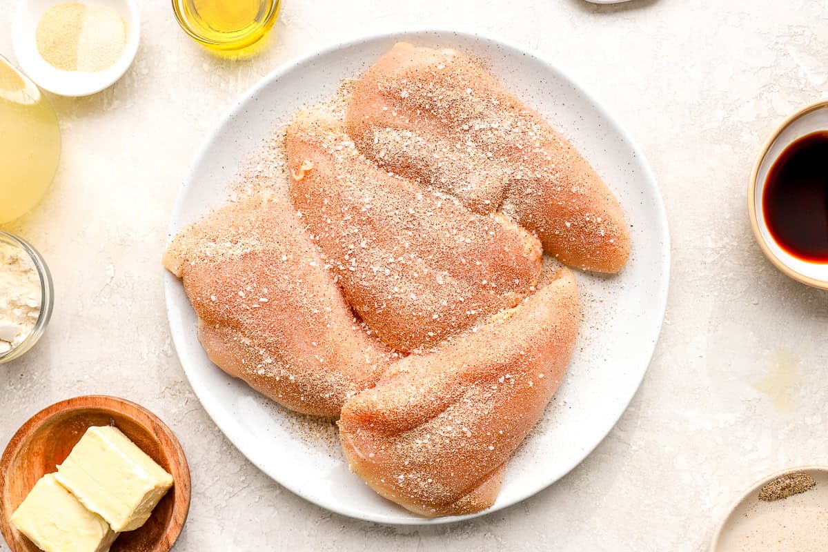 four seasoned raw chicken breasts on a white plate.