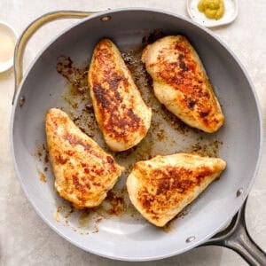 four seared seasoned chicken breasts in a skillet.