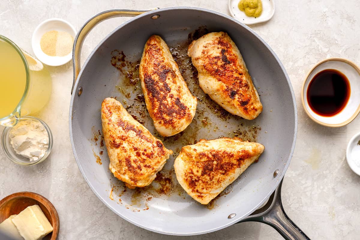 four seared seasoned chicken breasts in a skillet.
