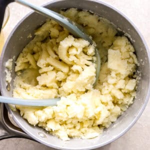 mashing potatoes in a saucepan with a potato masher.