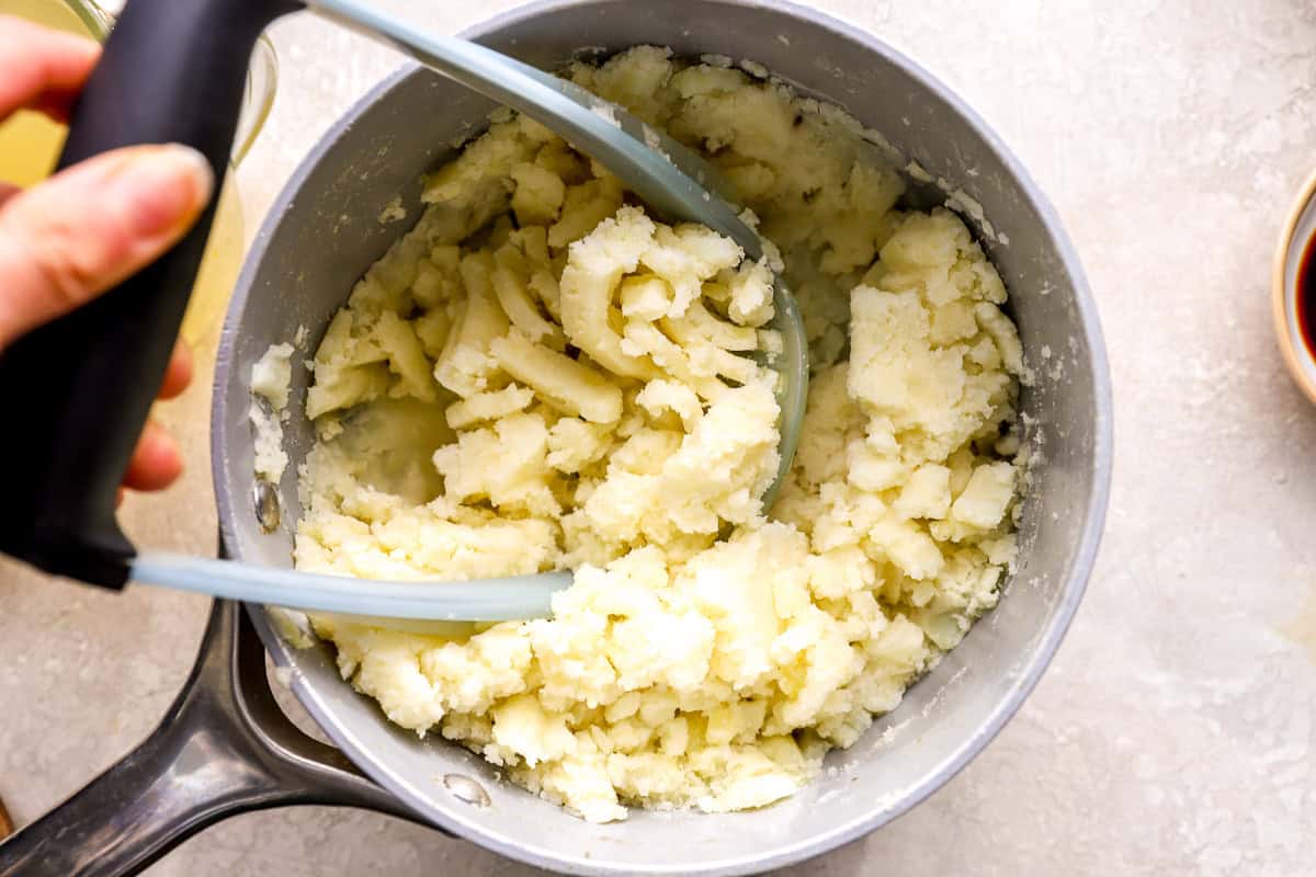 mashing potatoes in a saucepan with a potato masher.