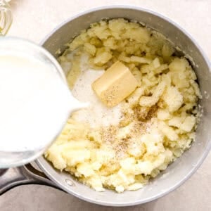 adding milk and butter to mashed potatoes in a saucepan.