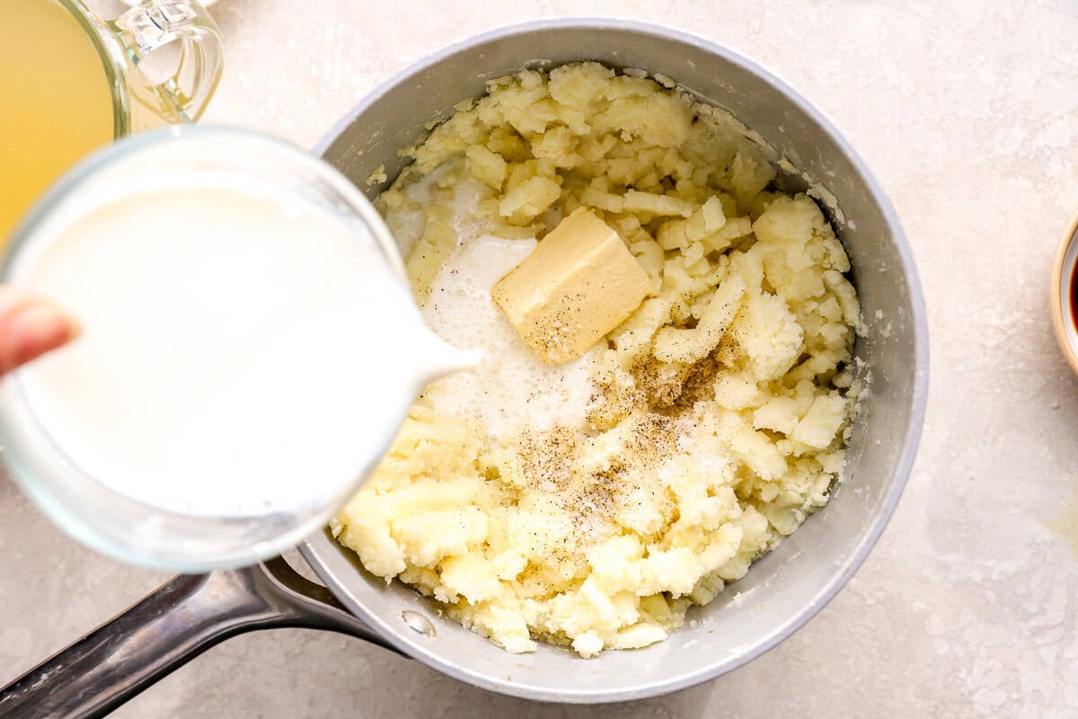 adding milk and butter to mashed potatoes in a saucepan.