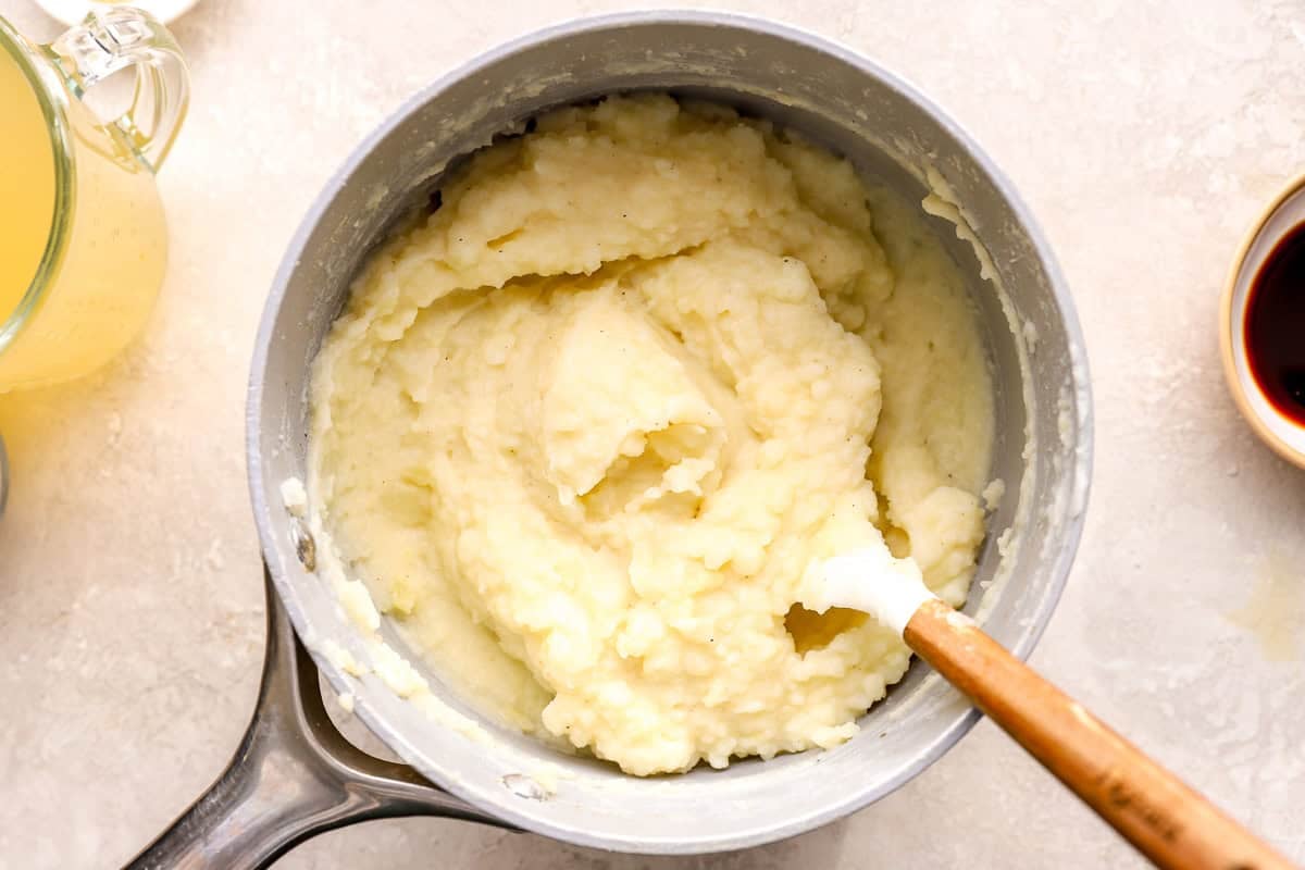 creamy mashed potatoes in a saucepan with a rubber spatula.