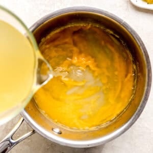 pouring chicken broth into a roux in a saucepan.