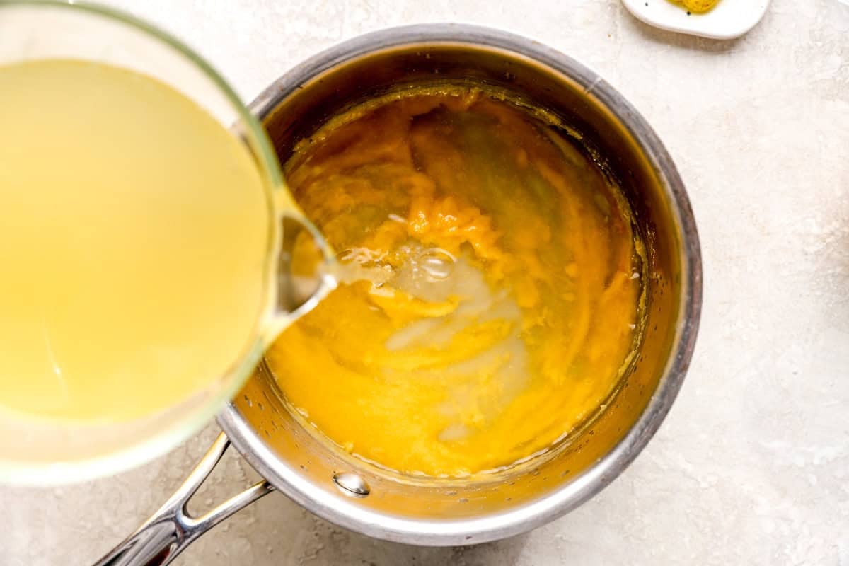 pouring chicken broth into a roux in a saucepan.