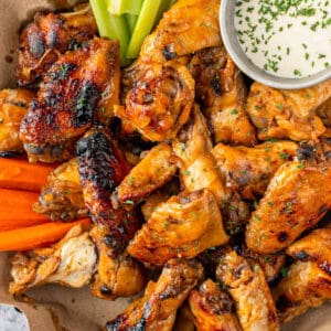 overhead view of crockpot bourbon chicken wings on a parchment-lined platter with carrot and celery sticks and ranch dip.