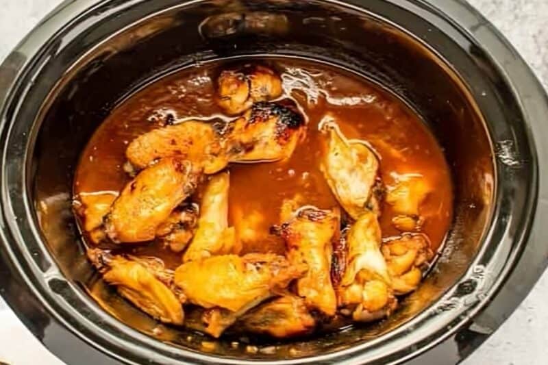 cooked and broiled chicken wings in bourbon sauce in a crockpot.