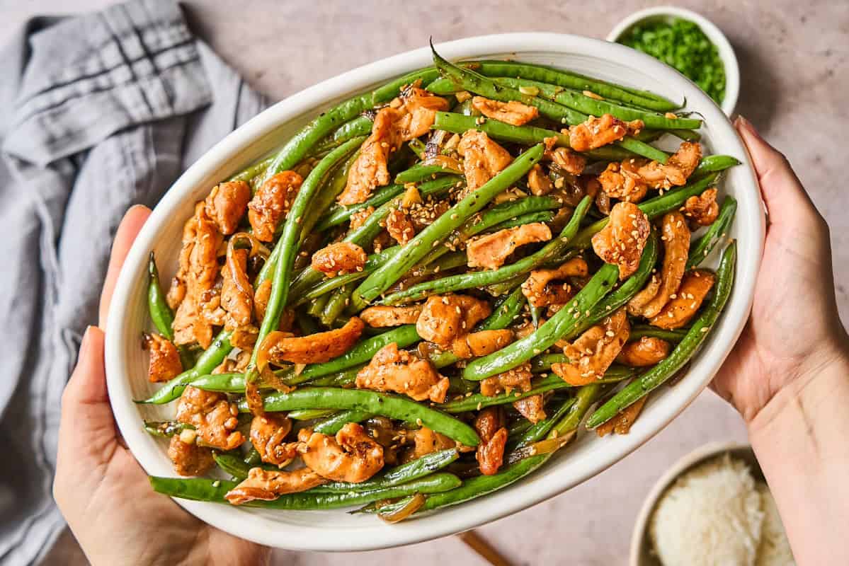 overhead view of chicken and green bean stir fry topped with sesame seeds in an oval serving dish.