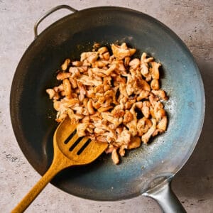 cooking chicken in a wok with a wooden spoon.