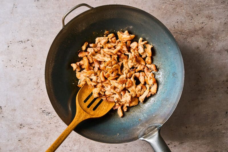 cooking chicken in a wok with a wooden spoon.