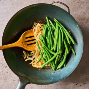 cooking onion and green beans in a wok with a wooden spoon.