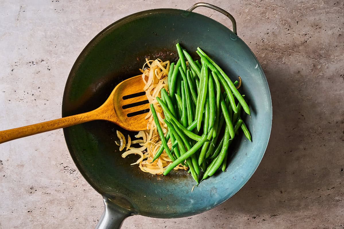 cooking onion and green beans in a wok with a wooden spoon.