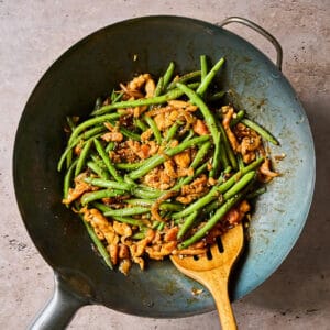 chicken and green bean stir fry with hoisin sauce in a wok with a wooden spoon.