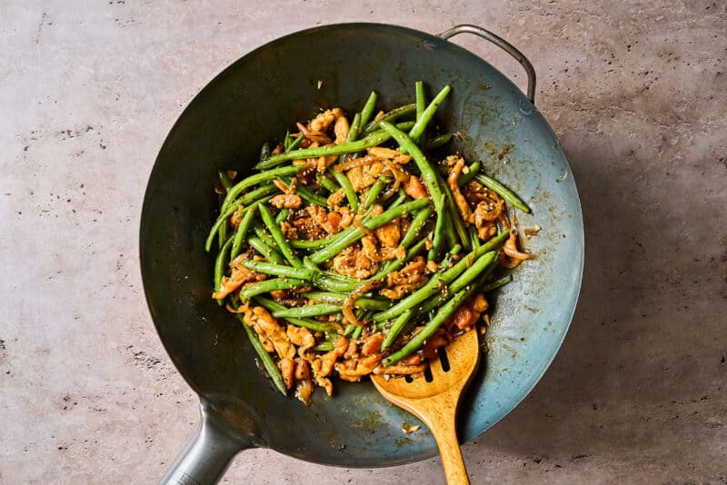 chicken and green bean stir fry with hoisin sauce in a wok with a wooden spoon.