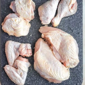 Raw whole chicken cut into pieces, arranged on a cutting board.