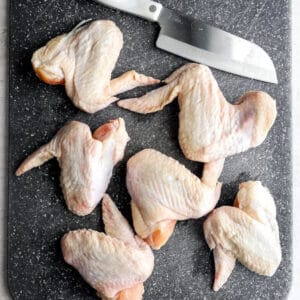 Whole chicken wings on a cutting board with a Chef's knife.